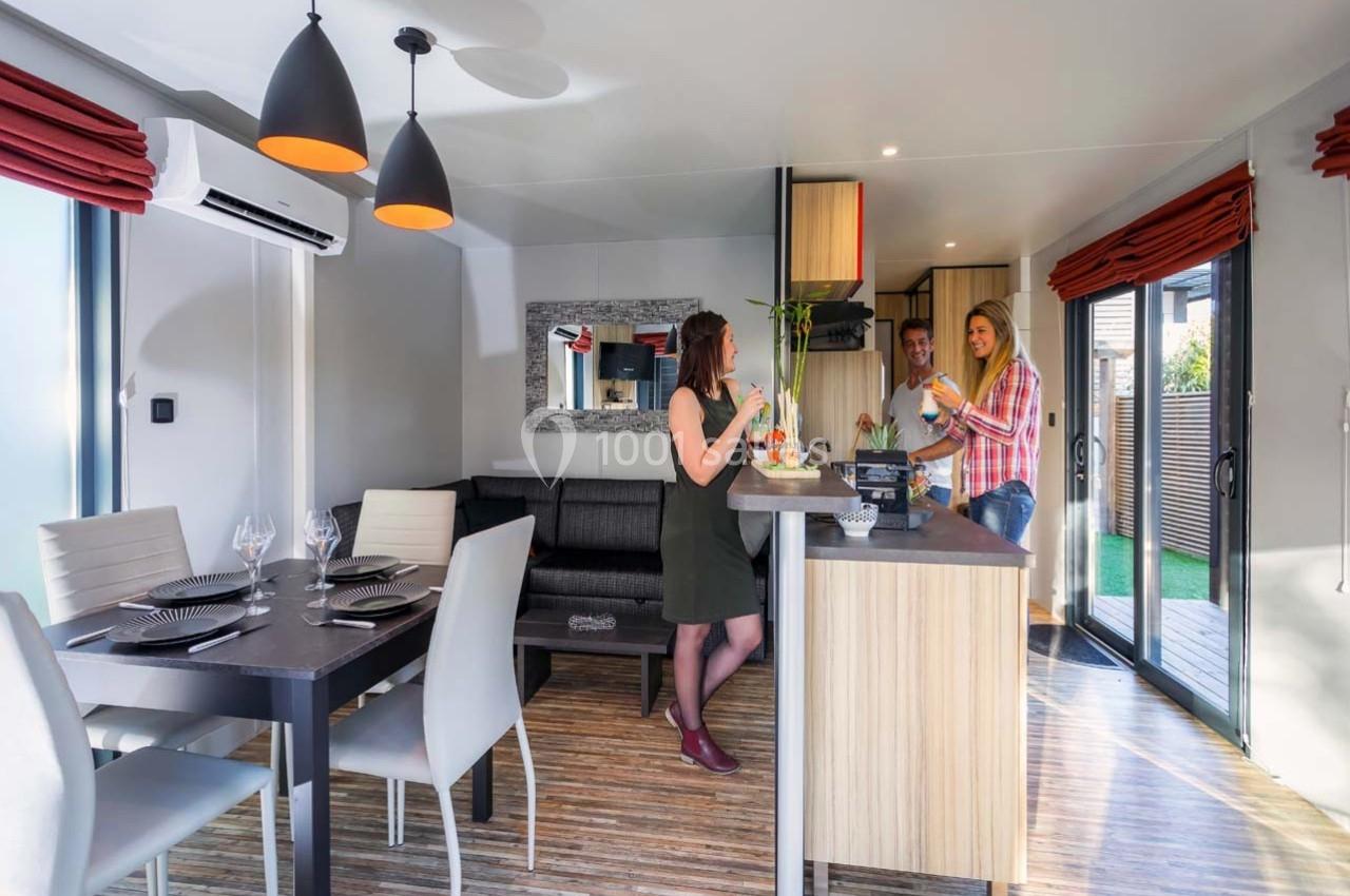 Intérieur lumineux d'un mobil-home avec trois personnes discutant près d'un comptoir, table dressée au premier plan.