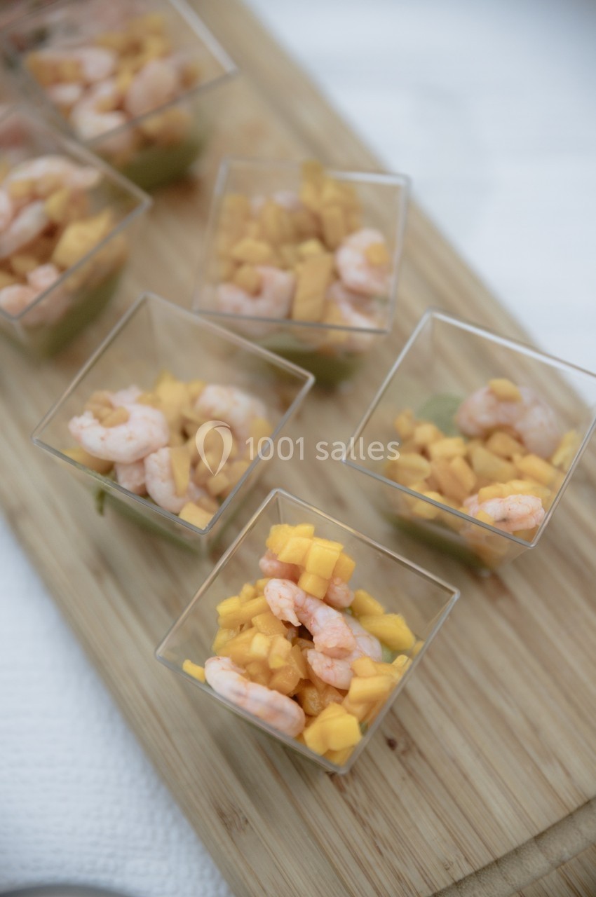 Verrines contenant des crevettes, dés de mangue et avocat, présentées sur une planche en bois.