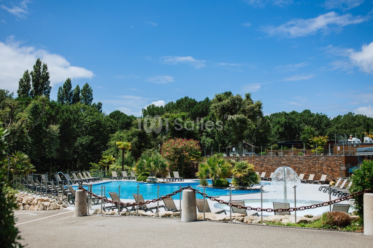 Piscine extérieure entourée de chaises longues, végétation luxuriante et ciel bleu en arrière-plan.