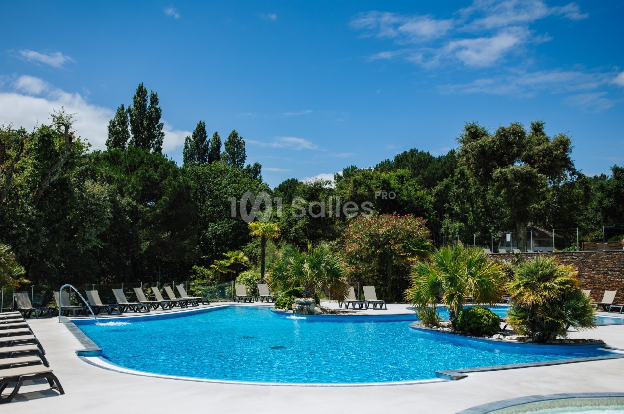 Piscine extérieure entourée de chaises longues, palmiers et végétation luxuriante sous un ciel bleu.