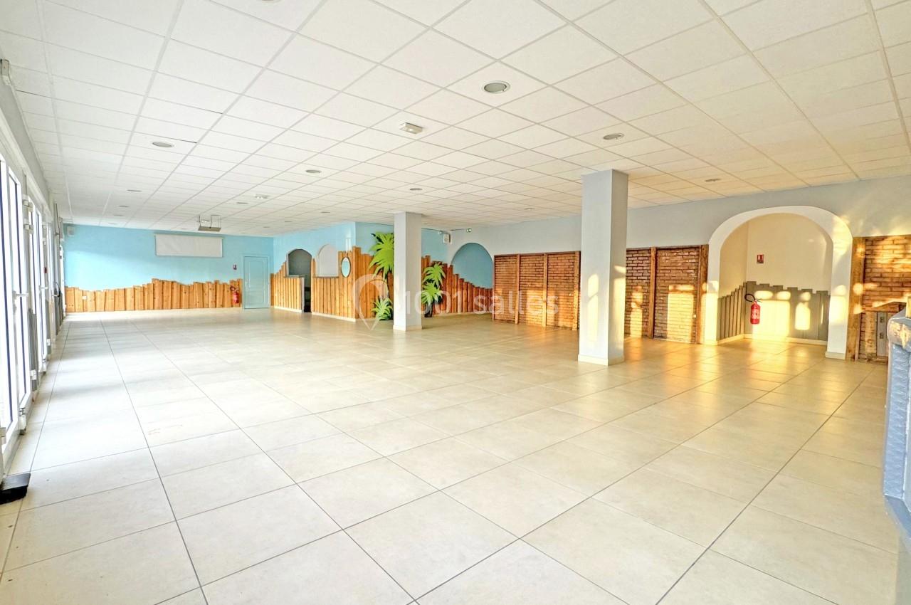 Salle spacieuse et lumineuse avec carrelage clair, murs décorés et grandes fenêtres laissant entrer la lumière naturelle.