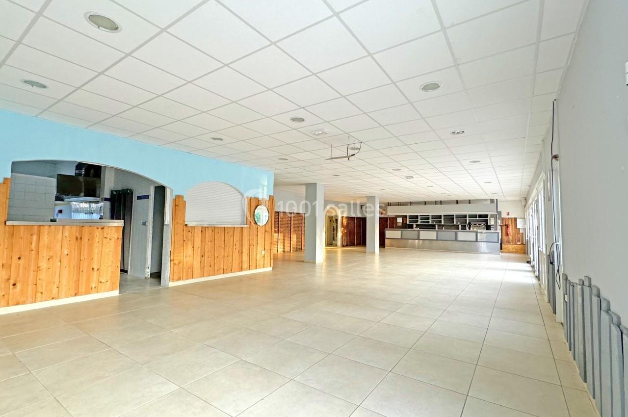 Salle spacieuse avec murs en bois et carrelage clair, équipée d'un comptoir et d'une cuisine ouverte en arrière-plan.