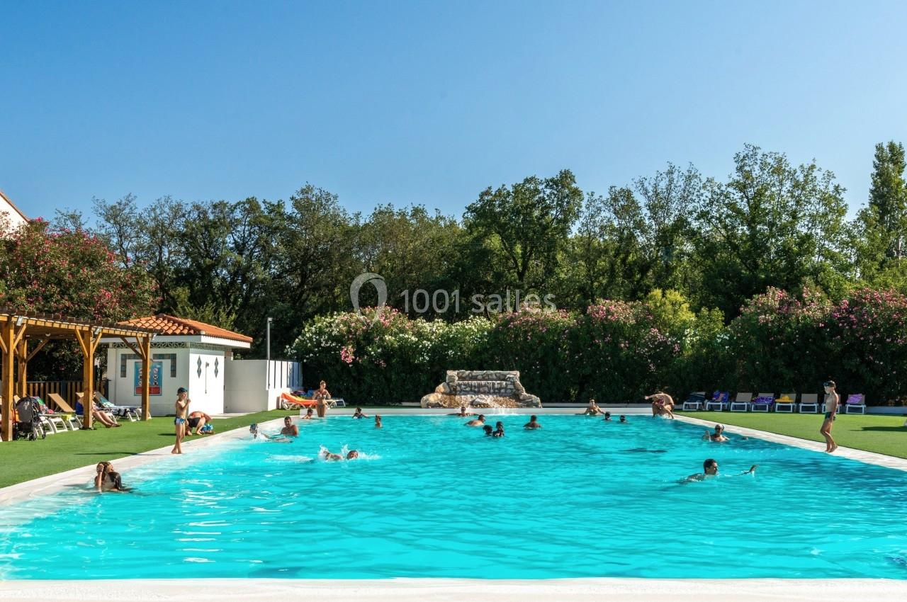 Piscine extérieure avec des baigneurs, entourée de végétation et de chaises longues sous un ciel dégagé.