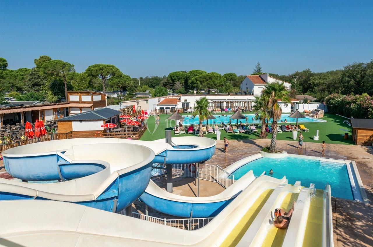 Vue d'un parc aquatique avec toboggans, piscine, transats et espaces verts sous un ciel dégagé.