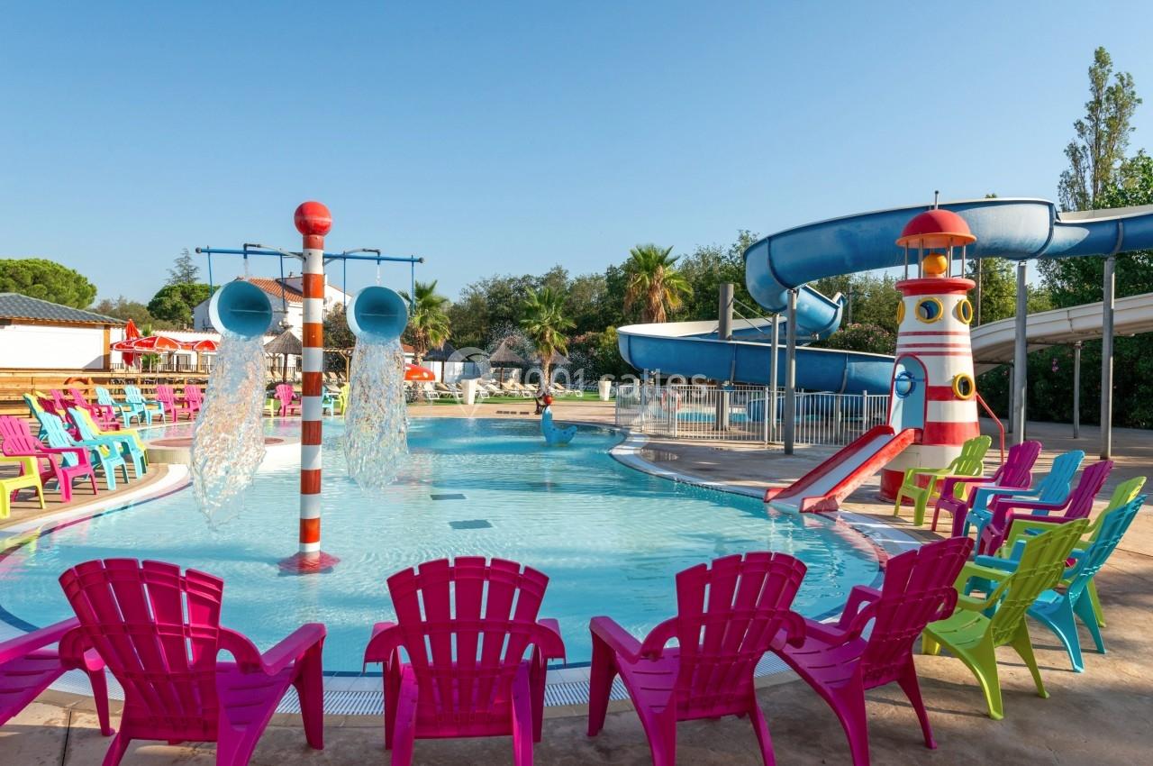 Piscine extérieure peu profonde avec jeux d'eau, toboggans et chaises colorées disposées autour.