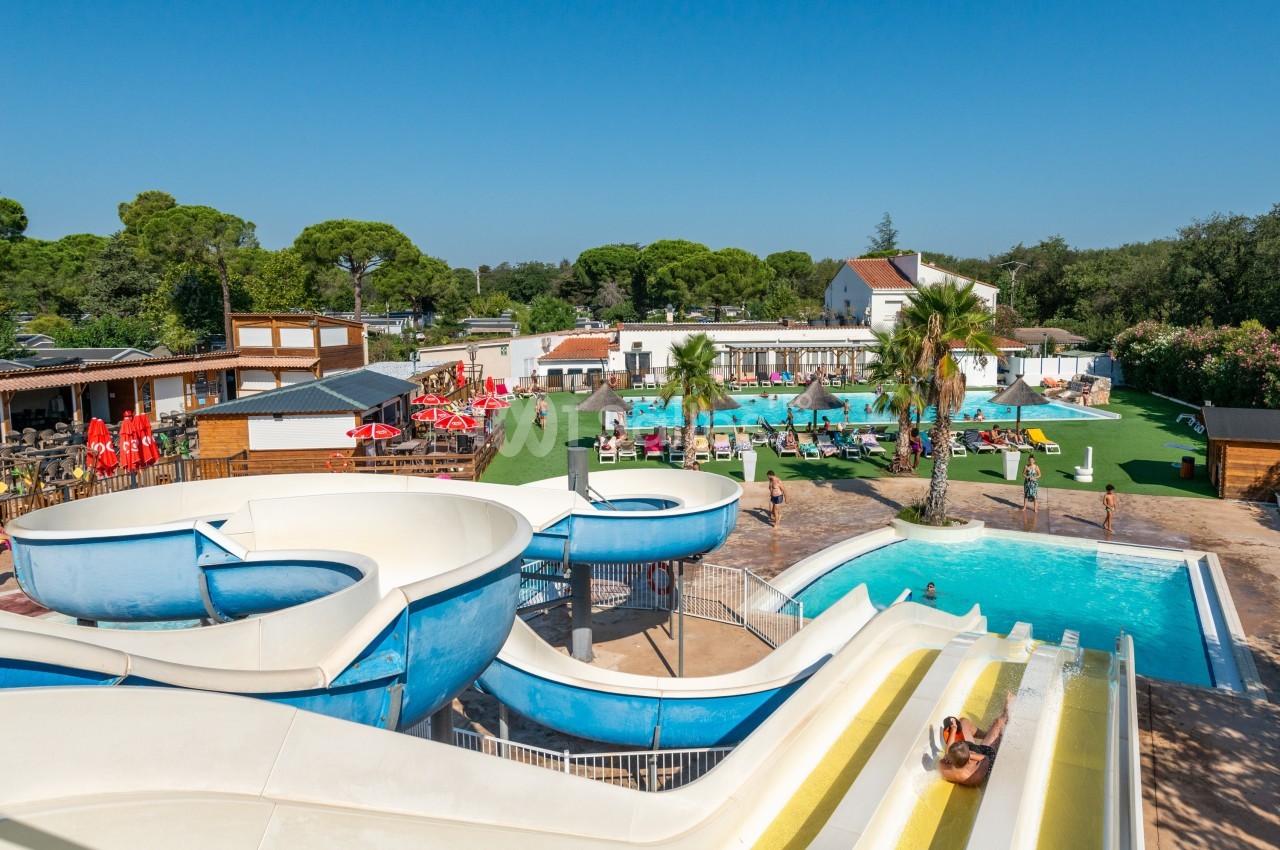 Vue d'un parc aquatique avec toboggans, piscine, transats et espaces verts sous un ciel dégagé.