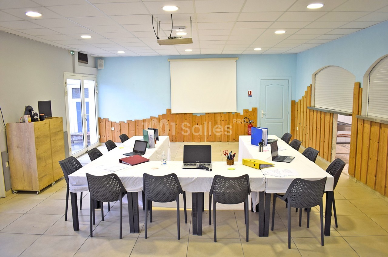 Salle de réunion équipée avec une grande table rectangulaire, des chaises, des ordinateurs et un projecteur.