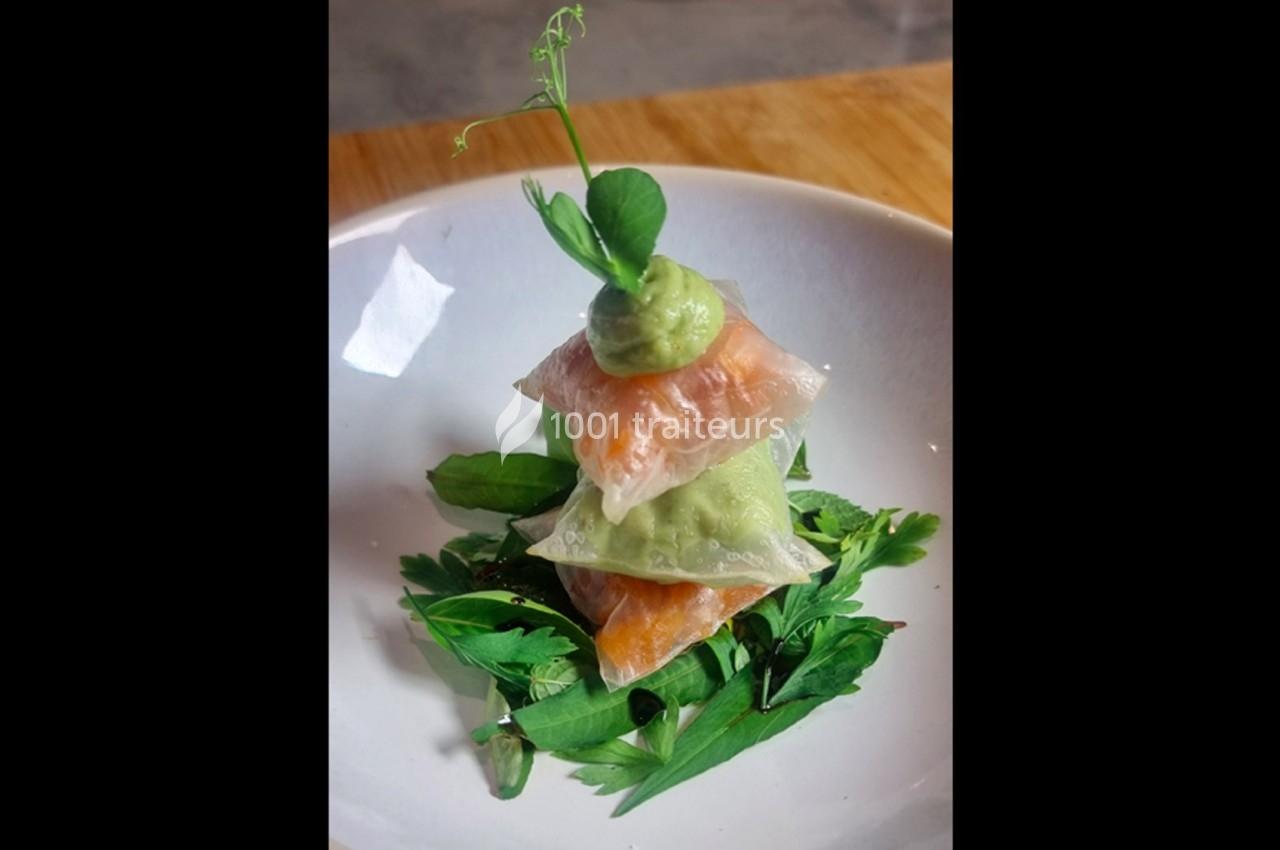 Empilement de ravioles transparentes garnies de saumon et d'avocat, décoré d'une pousse verte, sur un lit de verdure.