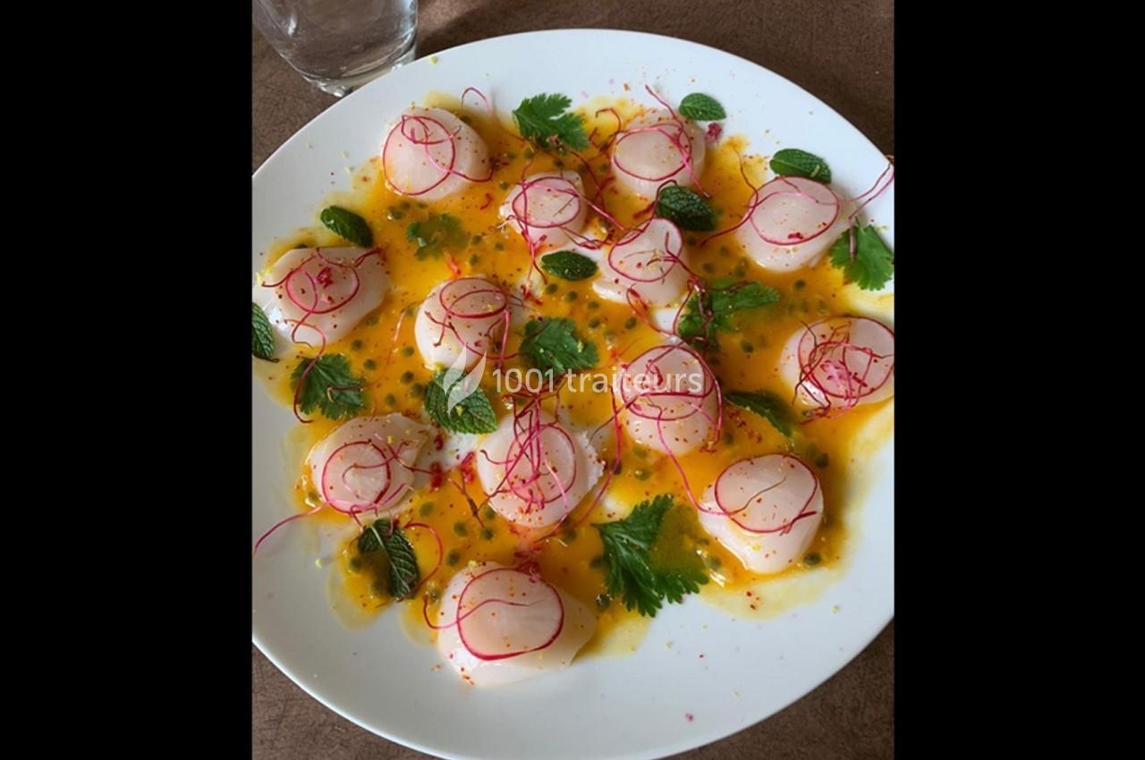 Assiette de carpaccio de Saint-Jacques avec sauce orange, radis tranchés, herbes fraîches et épices colorées.