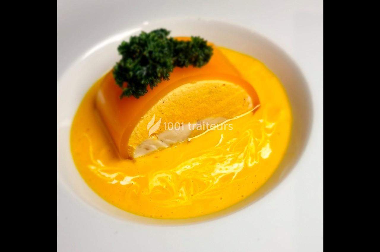 Part de mousse orange sur une sauce crémeuse jaune, garnie de persil frais, servie dans une assiette blanche.