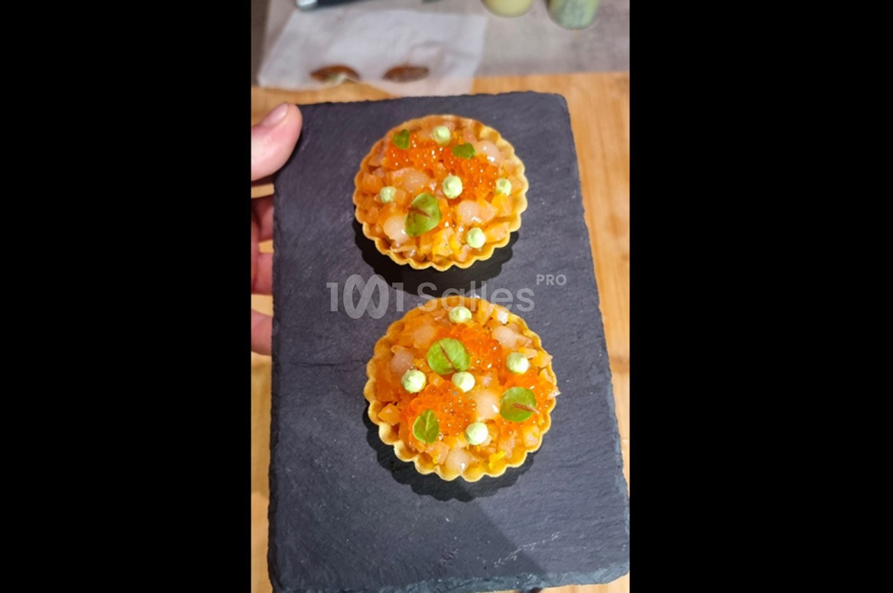 Deux tartelettes garnies de perles orange, crème et herbes fraîches, présentées sur une ardoise noire.
