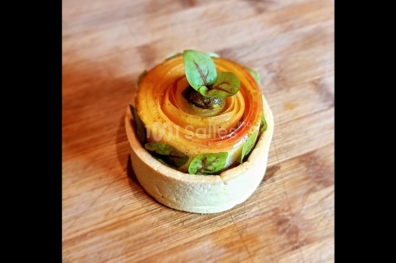 Tartelette garnie de fines tranches de fruits disposées en spirale, décorée de feuilles vertes sur une planche en bois.