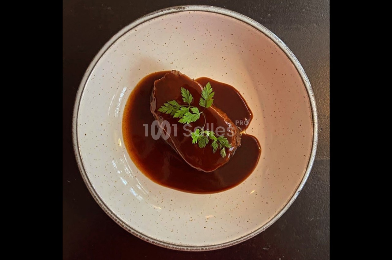 Plat de viande nappé de sauce brune, garni de feuilles de persil, présenté dans une assiette blanche.