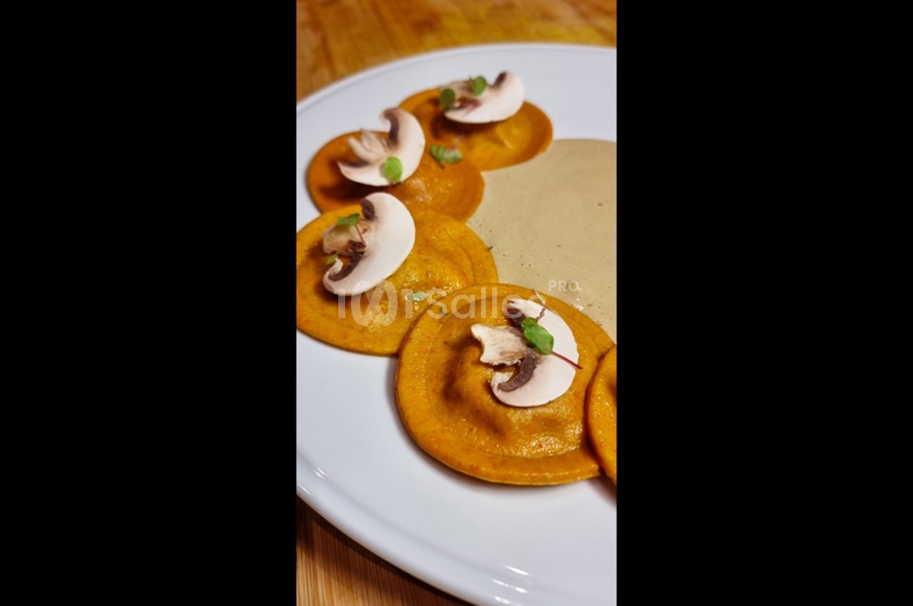 Assiette de ravioles orange garnies de champignons et herbes, accompagnées d'une sauce crémeuse beige.
