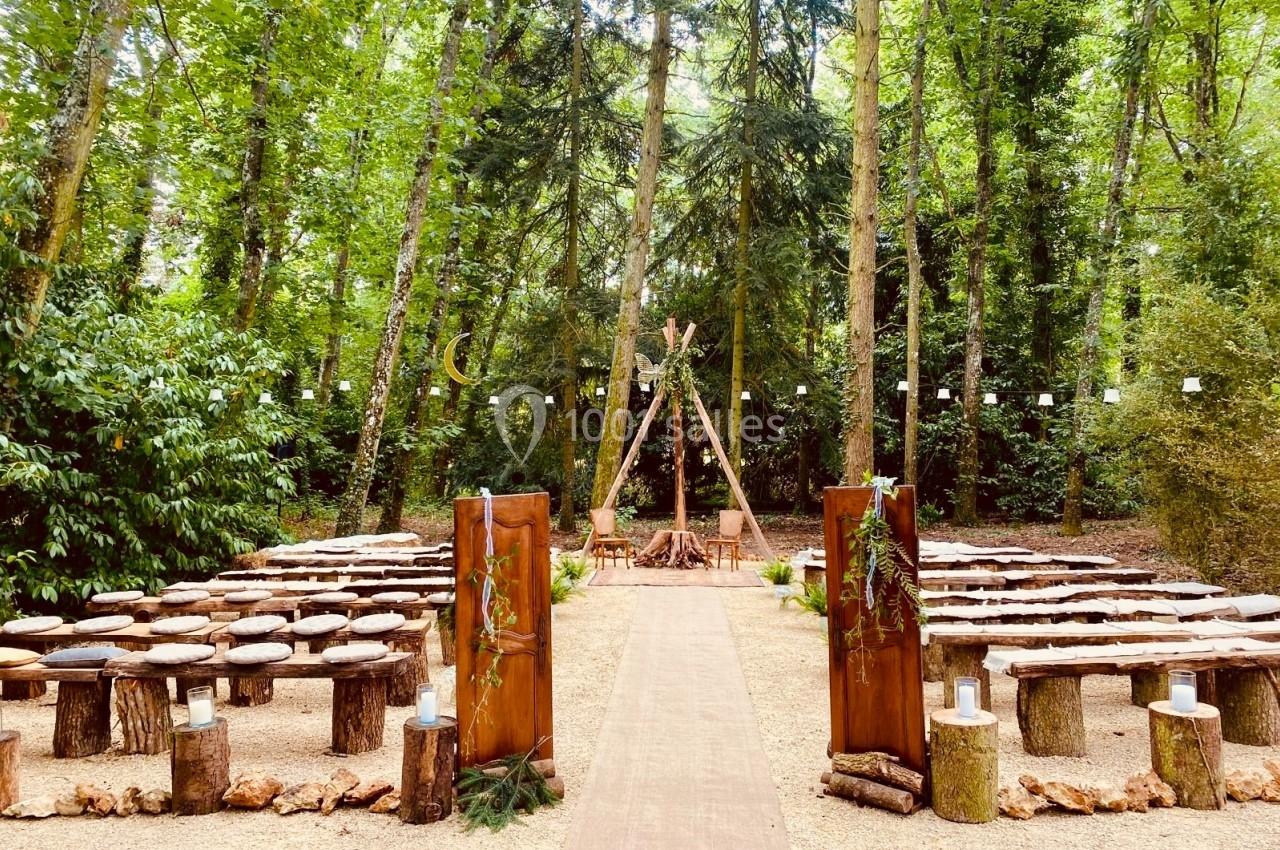 Allée centrale menant à une cérémonie en plein air dans une forêt, avec des bancs en rondins et une arche en bois.
