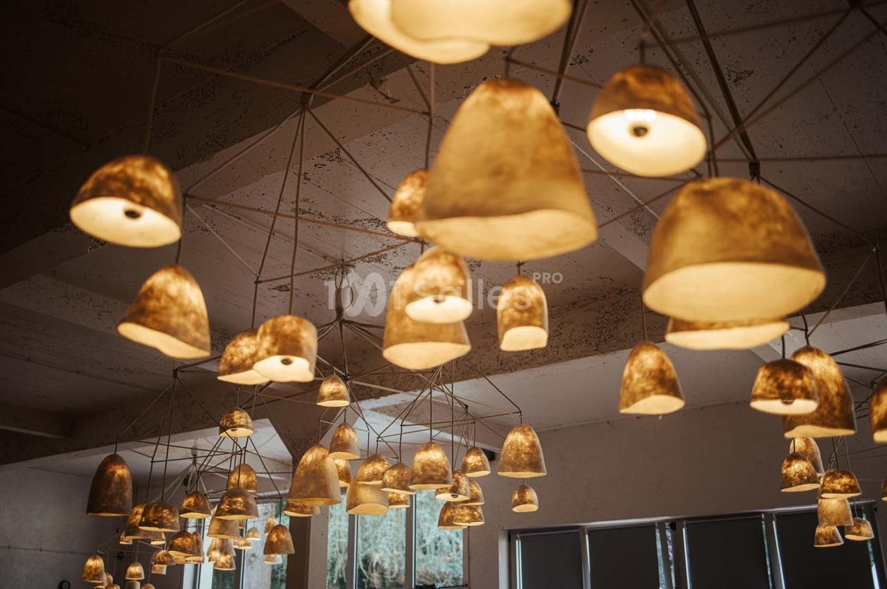 Suspension de multiples lampes en papier beige éclairées, accrochées à un plafond industriel.