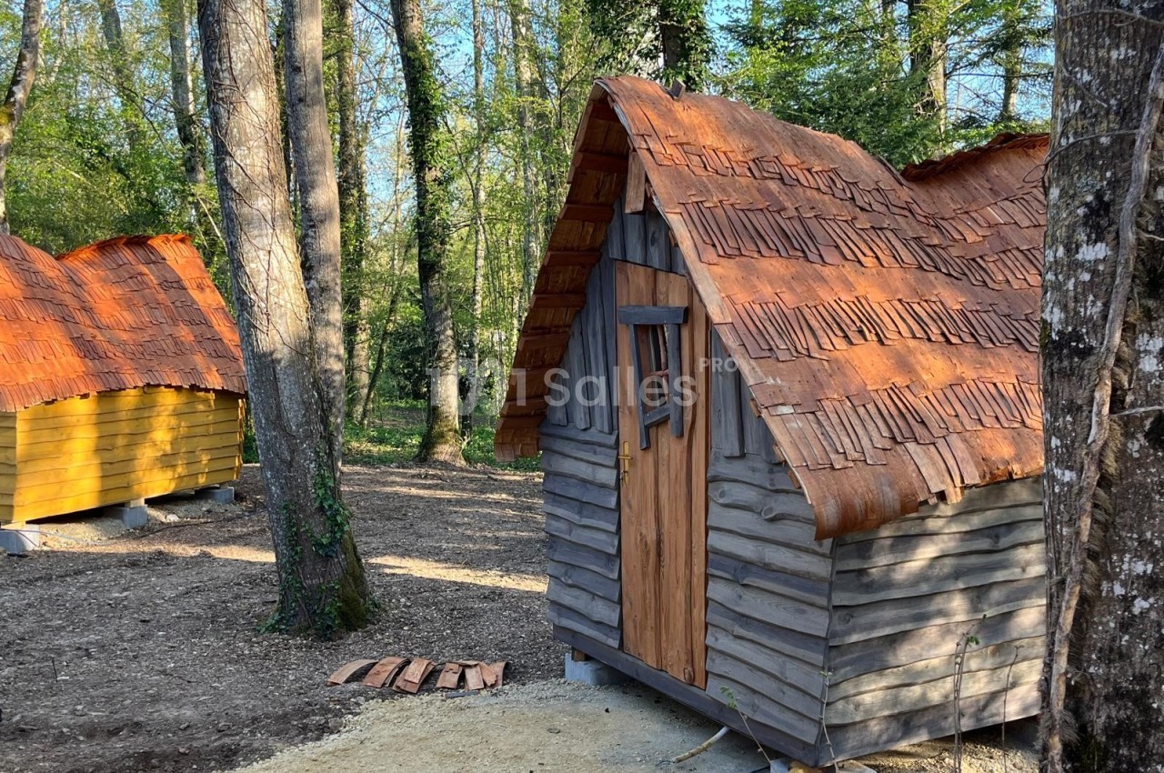 Petites cabanes en bois avec toits en tuiles dans une forêt, entourées d'arbres et de végétation.