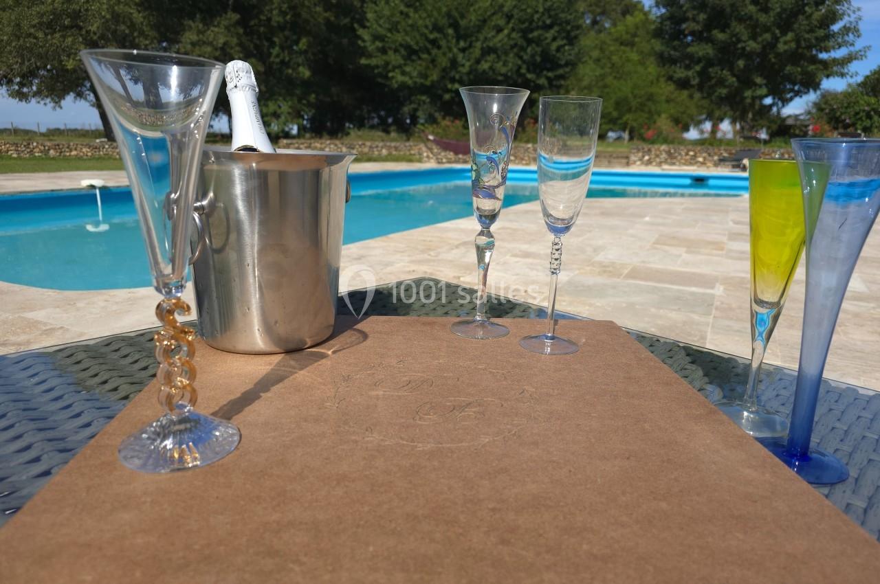 Verres à champagne et seau à glace sur une table près d'une piscine entourée de verdure.
