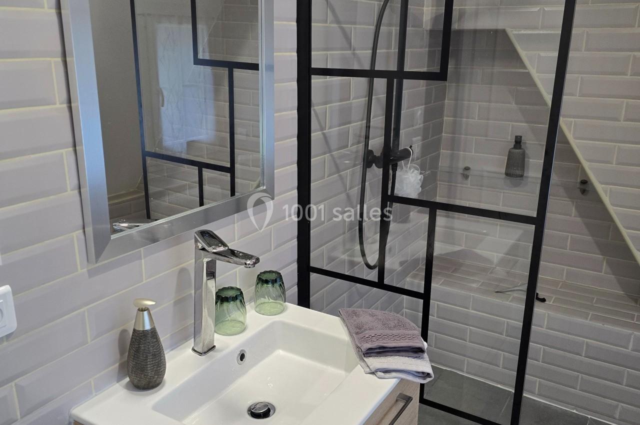 Salle de bain moderne avec lavabo, miroir, douche à paroi vitrée noire et carrelage mural blanc.
