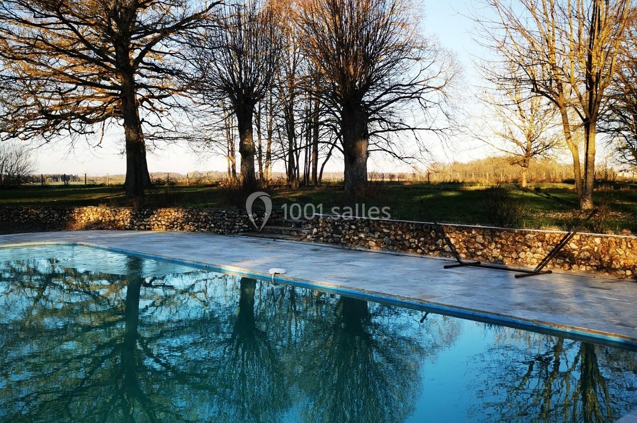 Piscine extérieure reflétant des arbres dénudés sous un ciel bleu clair en fin de journée.