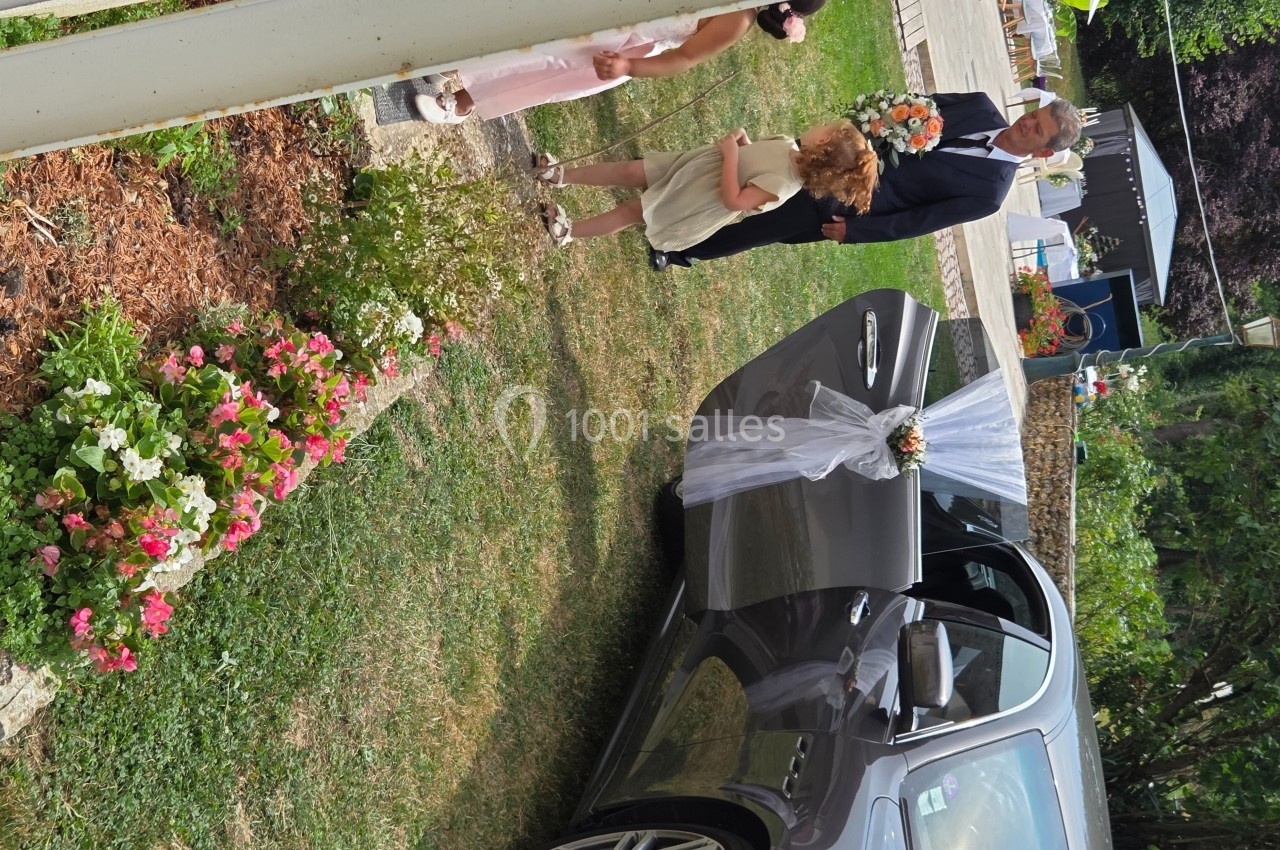 Un homme en costume sortant d'une voiture décorée pour un mariage, accompagné de deux enfants portant des fleurs.