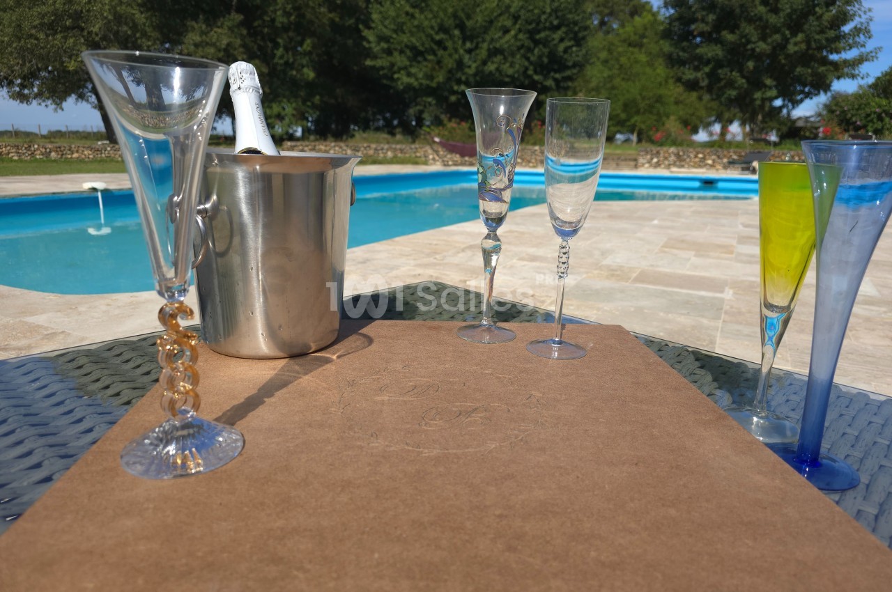 Seau à champagne, flûtes en verre et piscine en arrière-plan sur une terrasse ensoleillée.