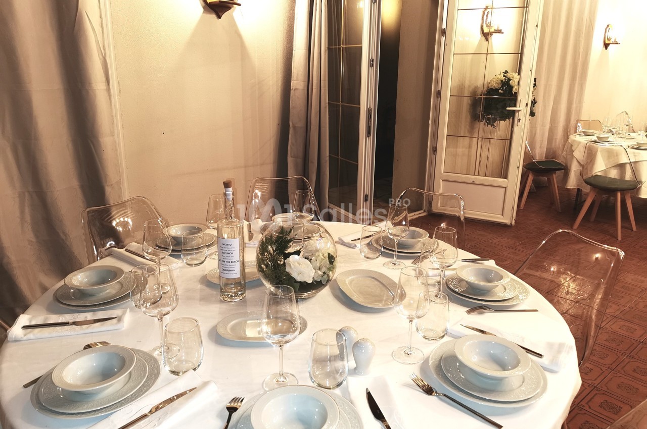 Table ronde dressée avec vaisselle blanche, verres et décoration florale, dans une salle lumineuse aux tons neutres.