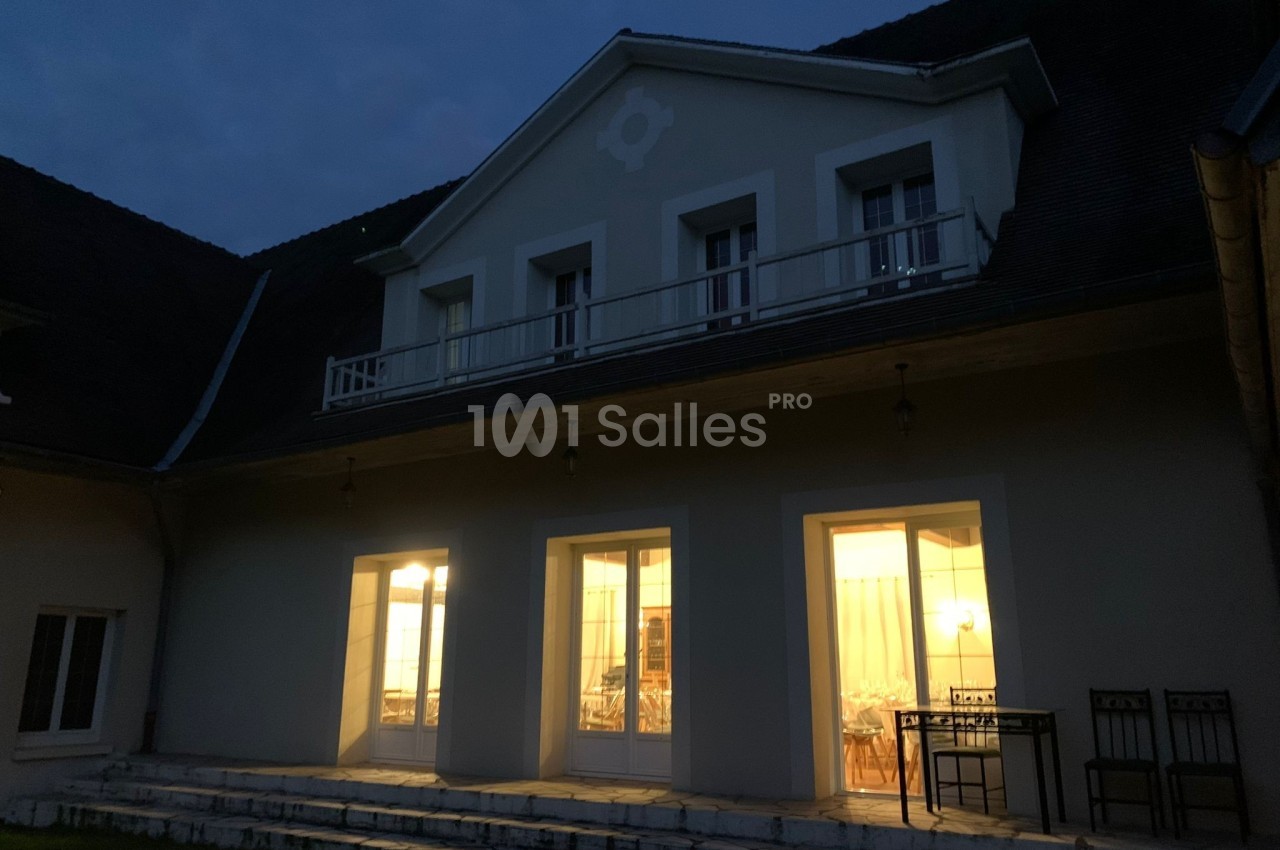 Façade d'une maison éclairée de nuit, avec des fenêtres et une porte-fenêtre donnant sur une terrasse.