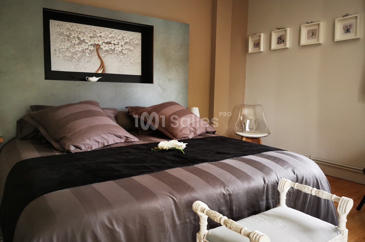 Lit double avec couvre-lit gris, coussins assortis, tableau floral en tête de lit et décoration minimaliste.