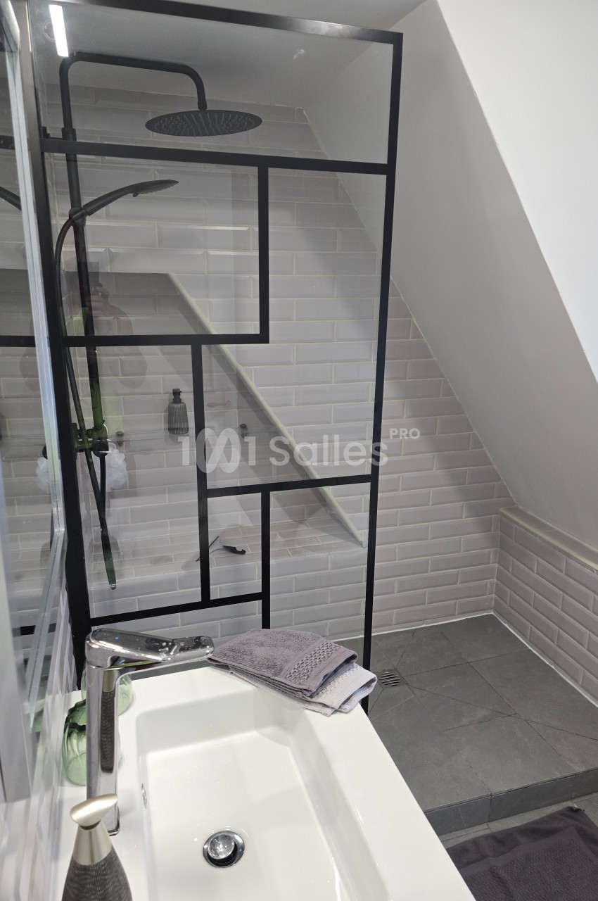 Salle de bain moderne avec douche à l'italienne, paroi vitrée à cadre noir, lavabo et carrelage blanc.