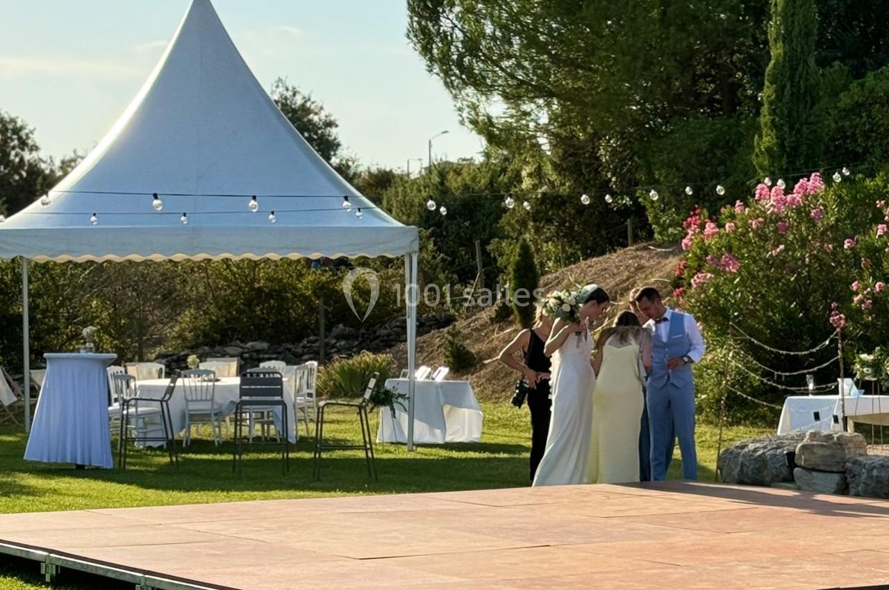 Un couple de mariés discute avec deux personnes près d'une tente blanche dans un jardin décoré pour une réception.