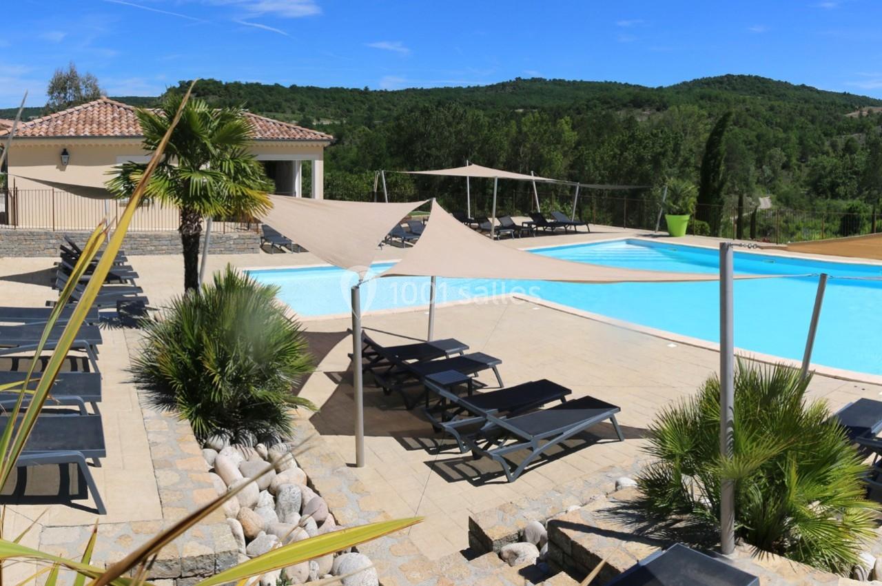Piscine extérieure avec transats, voiles d'ombrage et végétation, entourée de collines verdoyantes.