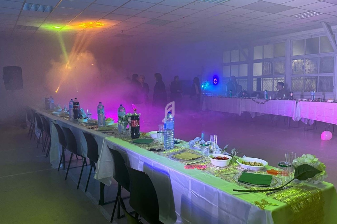 Salle décorée pour un événement avec tables dressées, éclairages colorés et ambiance enfumée.