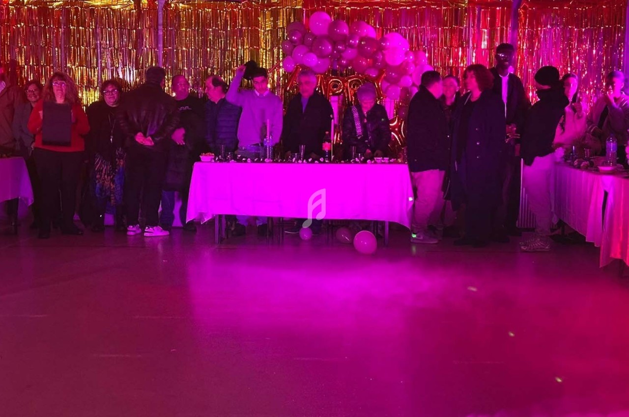 Groupe de personnes debout devant des tables décorées, dans une salle éclairée par des lumières roses et dorées.