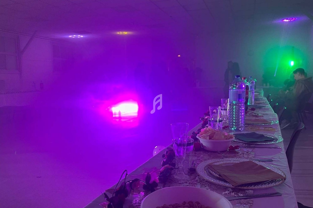 Salle de réception éclairée par des lumières colorées, avec une longue table dressée au premier plan.