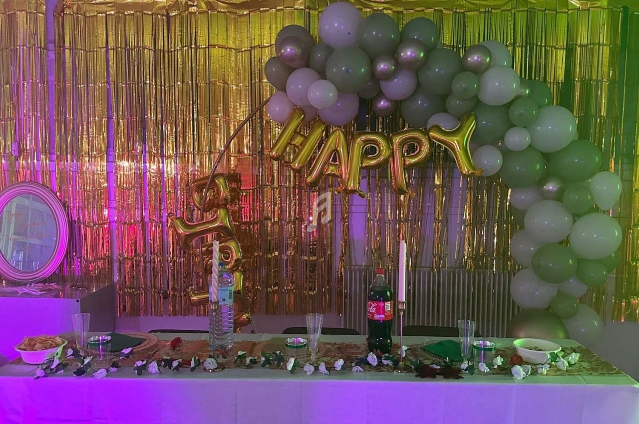 Décoration de fête avec ballons verts et dorés, guirlande ’Happy’, table dressée avec boissons et snacks.