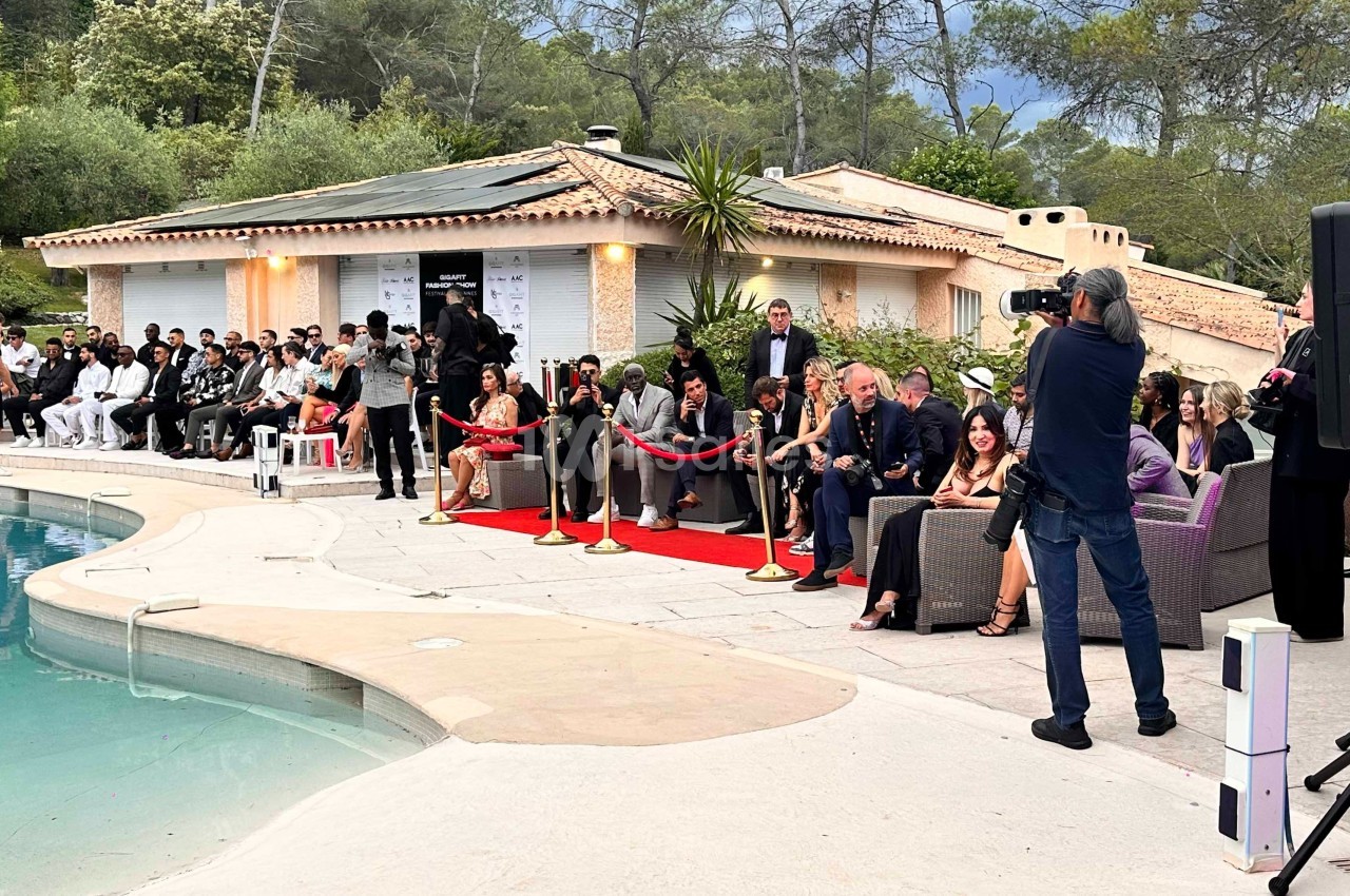 Un photographe capture un événement en plein air près d'une piscine, avec des invités assis et un tapis rouge.