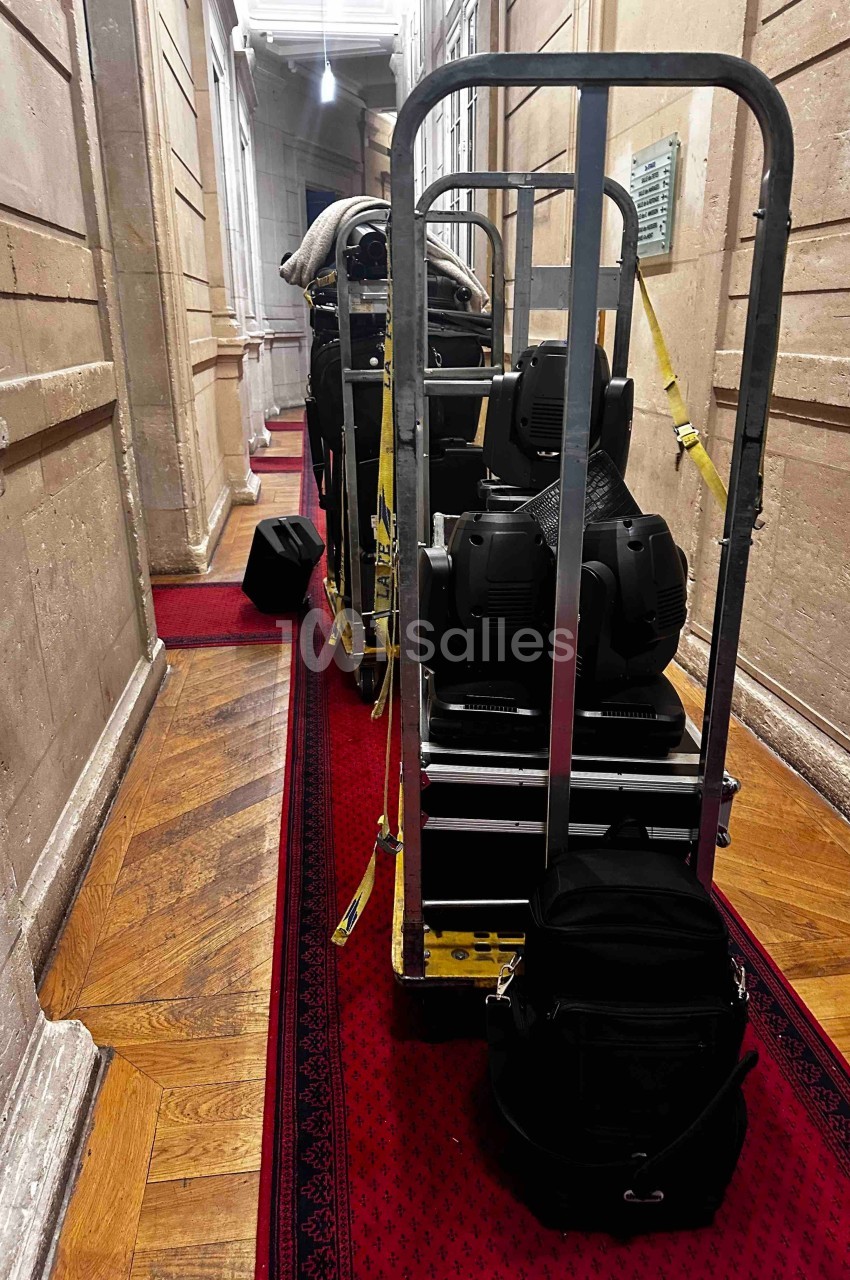 Chariot chargé de matériel technique sur un tapis rouge dans un couloir aux murs en pierre.