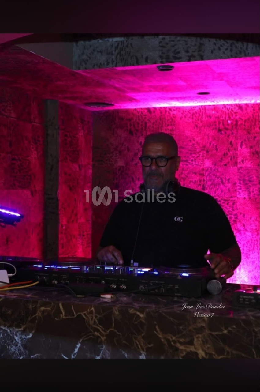 DJ en console de mixage dans un espace aux murs illuminés en rose vif avec éclairage bleu d'ambiance.