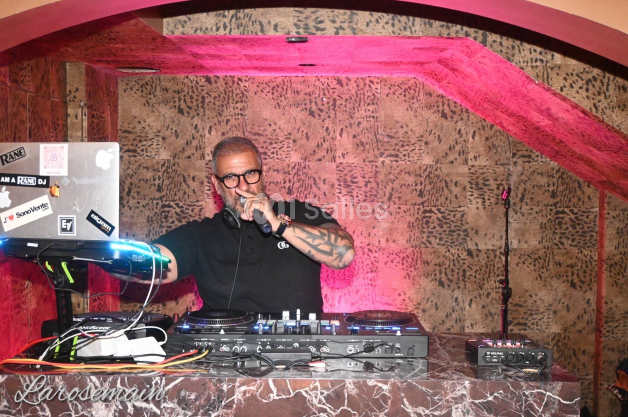 DJ en cabine sous éclairage rose vif, murs en pierre brute, équipement de sonorisation visible.