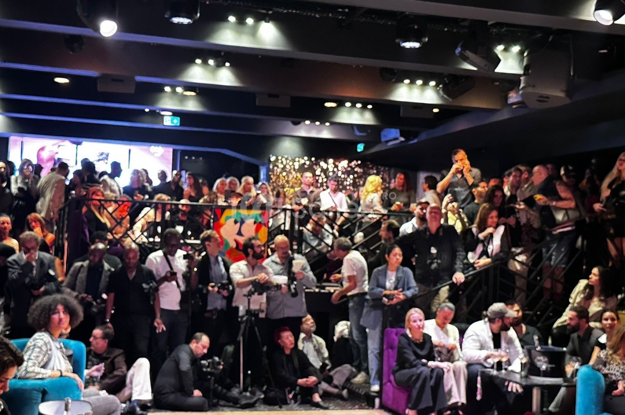 Salle bondée avec des personnes debout et assises, éclairage tamisé, ambiance animée lors d'un événement.