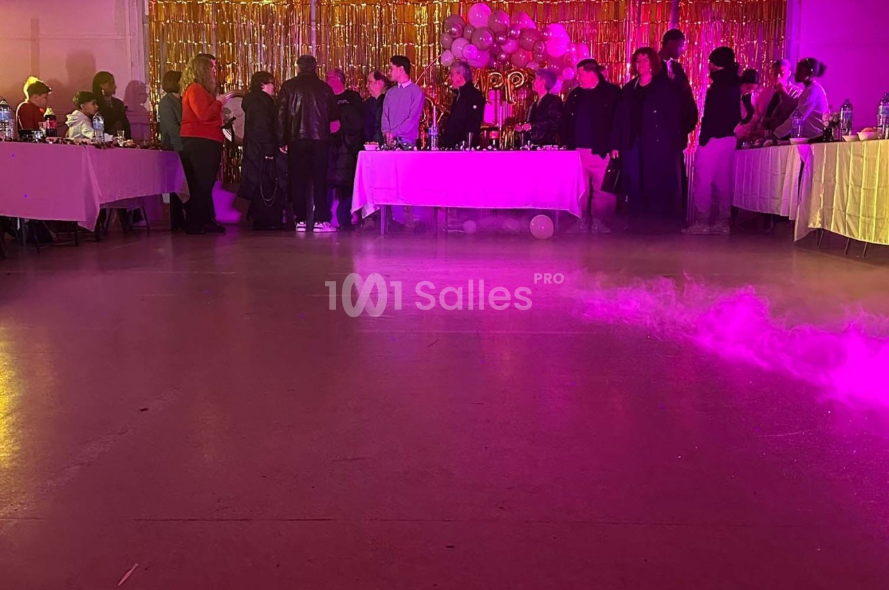Des personnes rassemblées dans une salle décorée avec des ballons et des guirlandes dorées, éclairée par des lumières…
