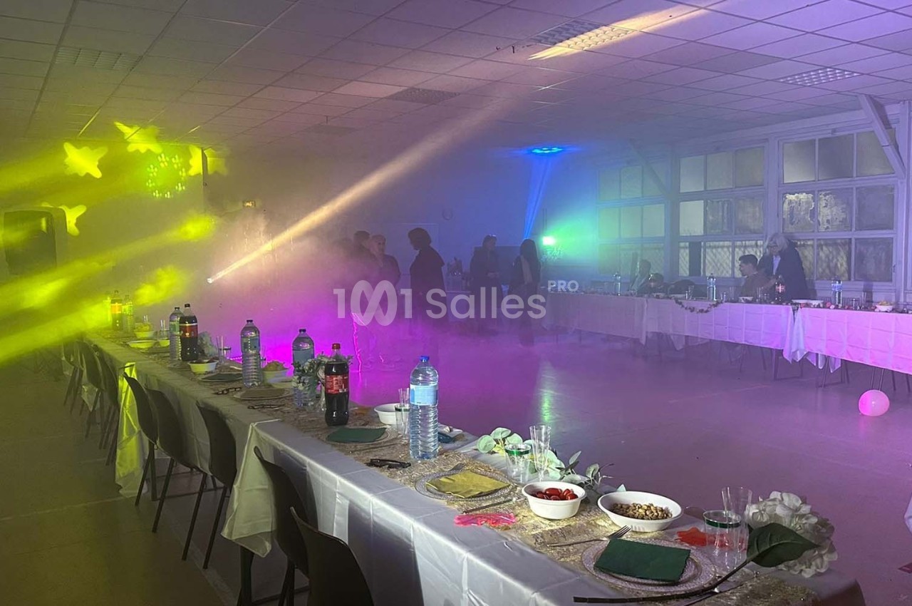 Salle décorée pour un événement avec tables dressées, éclairages colorés et fumée créant une ambiance festive.