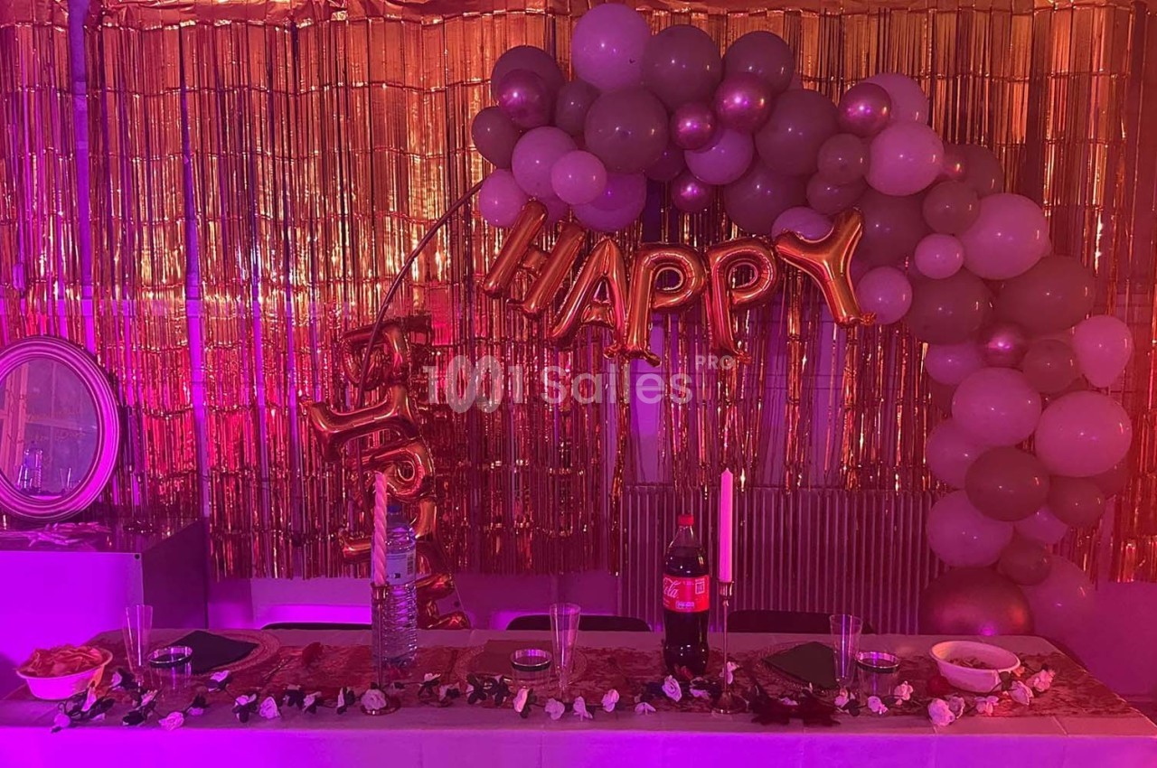 Décoration festive avec ballons, guirlandes dorées et table dressée contenant boissons, bougies et collations.