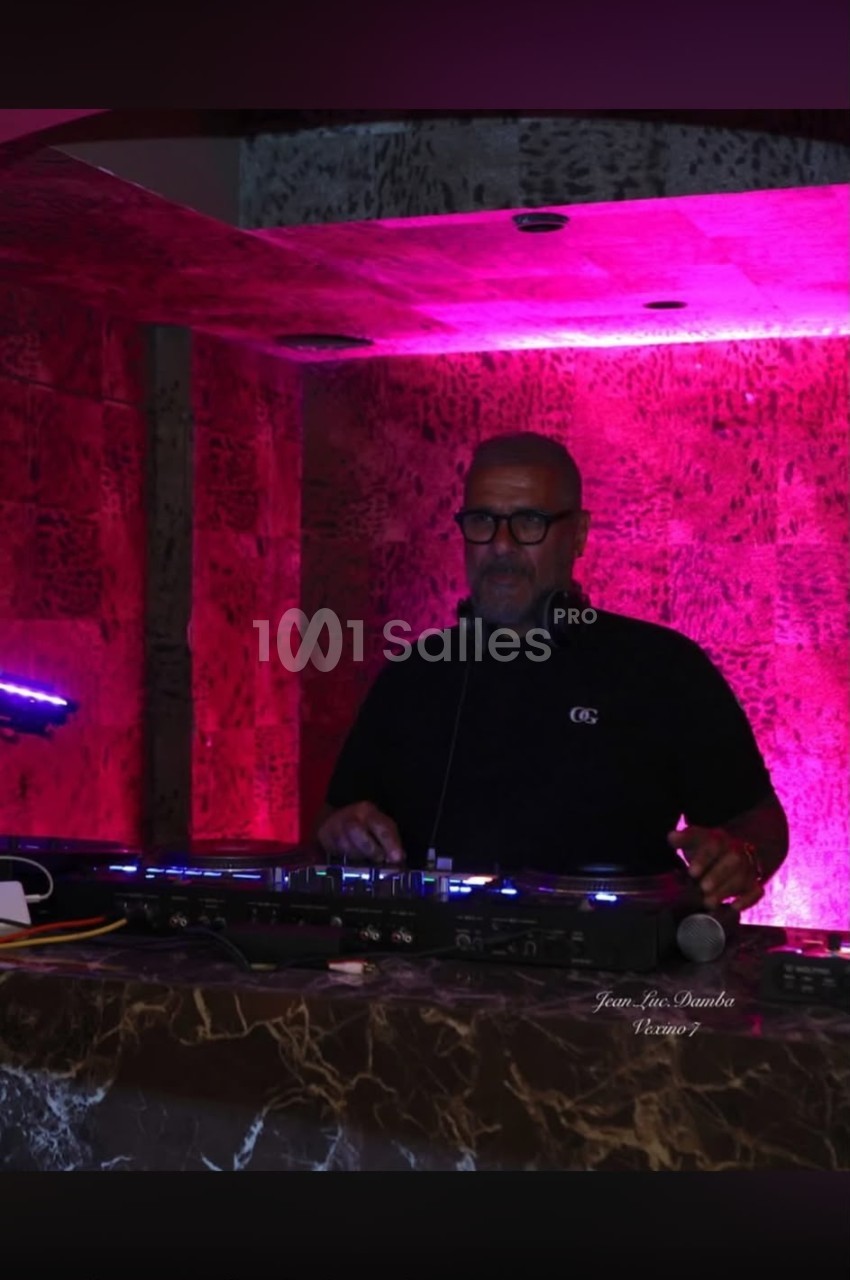 DJ en console de mixage dans un espace aux murs illuminés en rose vif avec éclairage bleu d'ambiance.