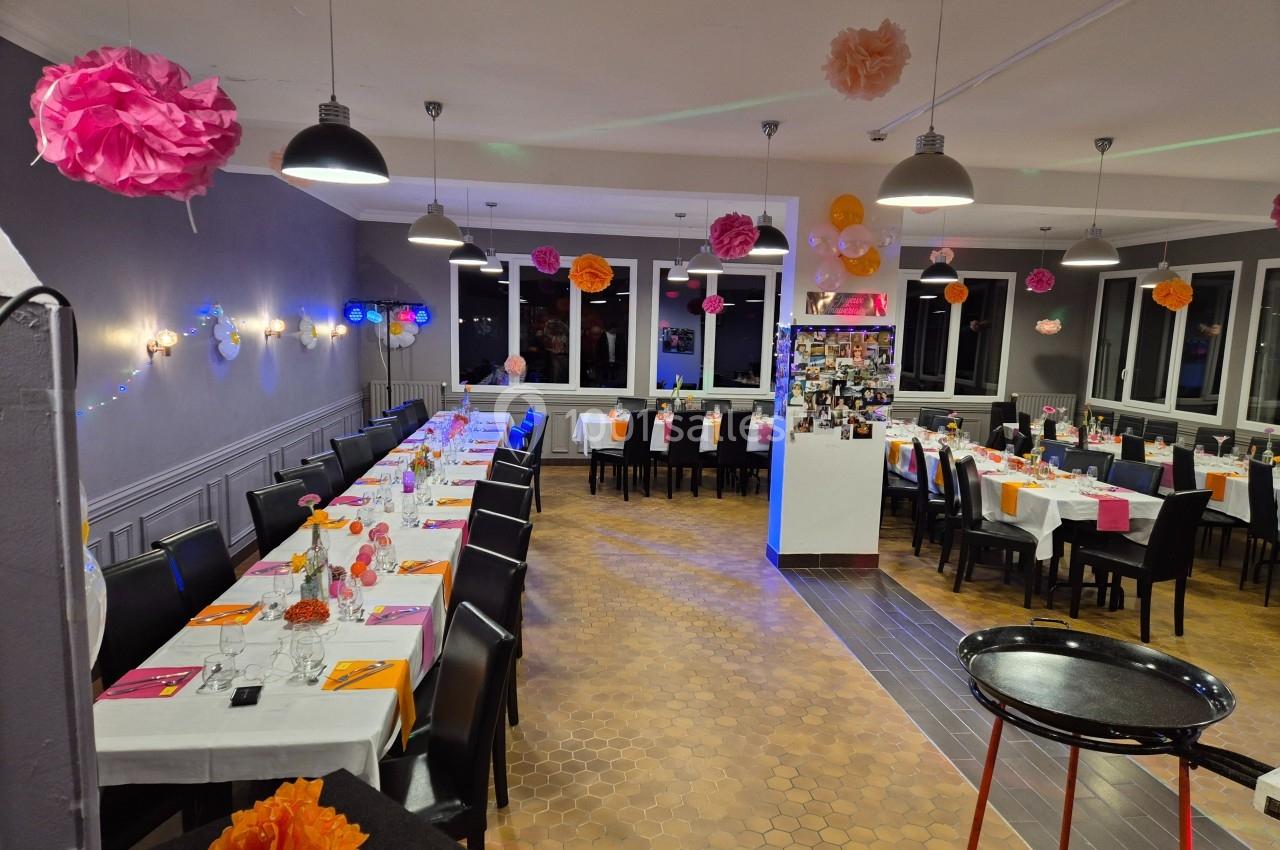 Salle décorée pour un événement, avec tables dressées, chaises noires et suspensions colorées.