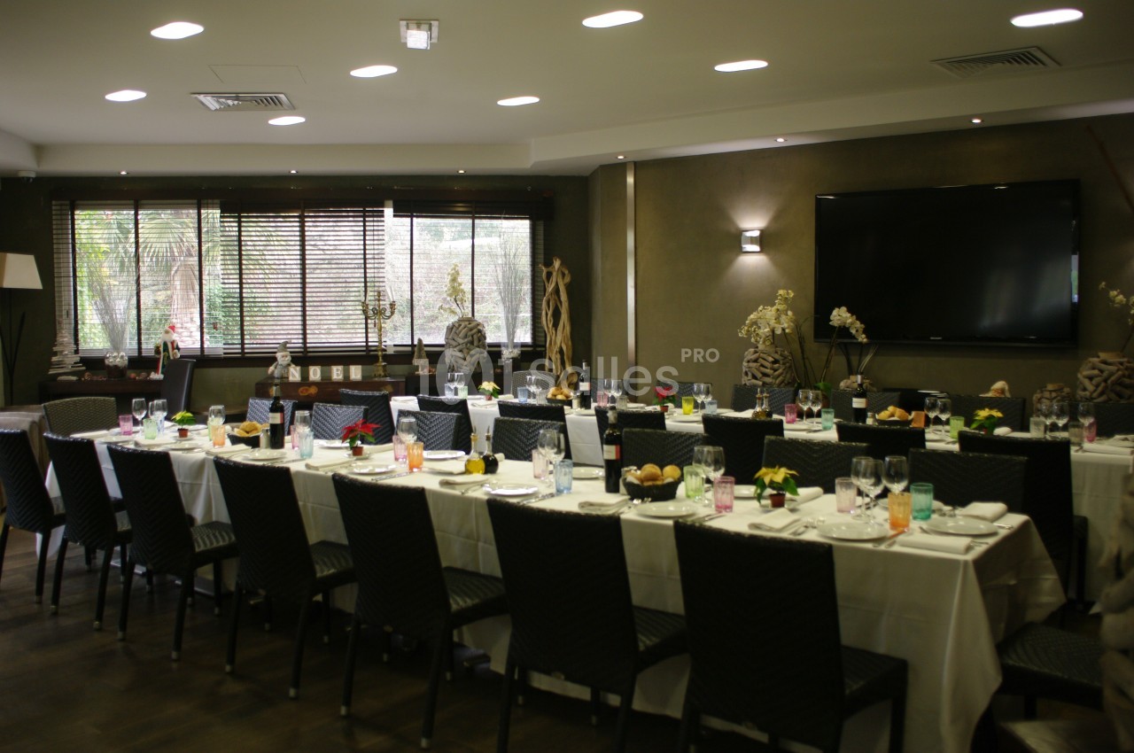 Salle de réception avec de longues tables dressées pour un repas, éclairée par des fenêtres et des luminaires modernes.