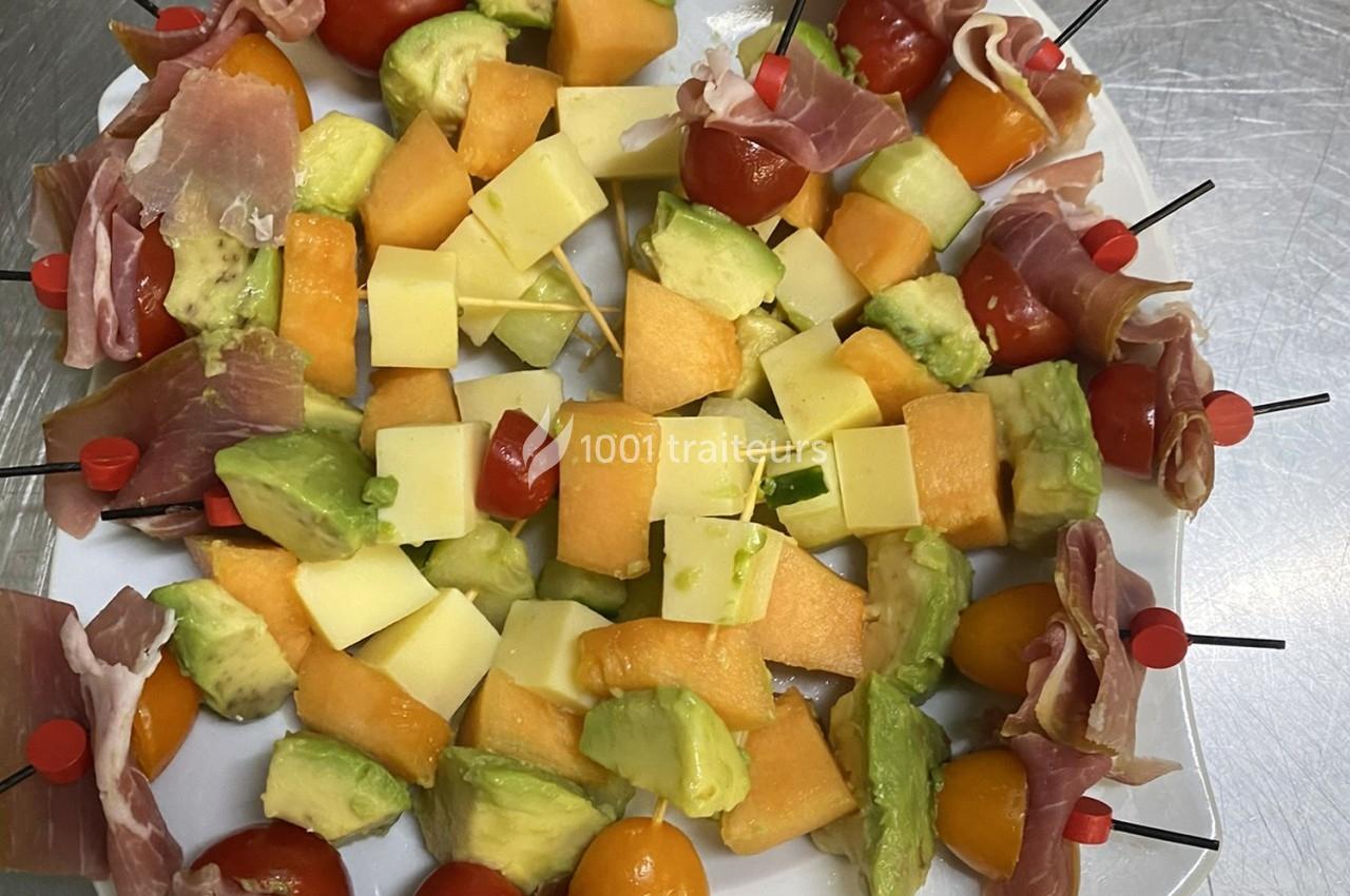 Assortiment de brochettes apéritives avec melon, avocat, fromage, tomates cerises et jambon cru sur un plateau.