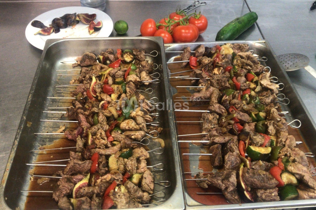 Brochettes de viande et légumes colorés disposées sur des plateaux en cuisine, avec des légumes frais en arrière-plan.