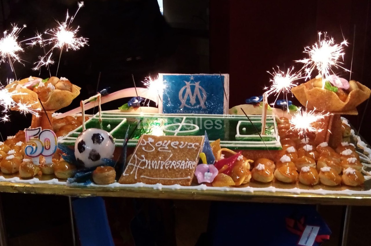 Gâteau d'anniversaire en forme de terrain de football, décoré de choux, d'étincelles et d'éléments sur le thème de l'OM.